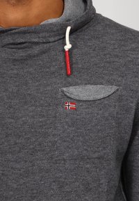 Sweat à capuche gris à finition texturée, avec une poche avant, un petit emblème du drapeau norvégien et un cordon blanc avec des embouts rouges.