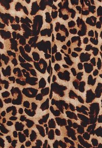 O tecido com padrão de leopardo possui um fundo bege com grandes manchas irregulares pretas e castanhas. A textura parece suave com um leve brilho.