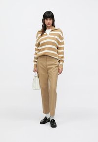 Bež i bijeli prugasti džemper s patentnim zatvaračem, bež hlače, bijela torbica, crne cipele, svijetlosive čarape; opušteni kroj i ležerni stil.