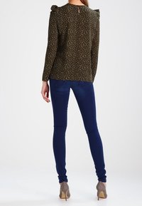 Blusa verde scuro con motivo floreale bianco, maniche a sbuffo e dettaglio a chiave sul retro, abbinata a jeans skinny blu scuro e tacchi color taupe.