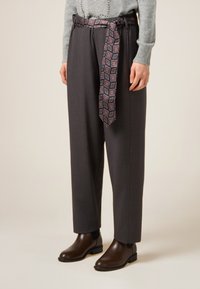 Pantaloni grigi su misura con una cintura larga decorata da una cintura con motivo. Abbinati a stivaletti marroni lucidi. Maglione morbido lavorato a maglia visibile.