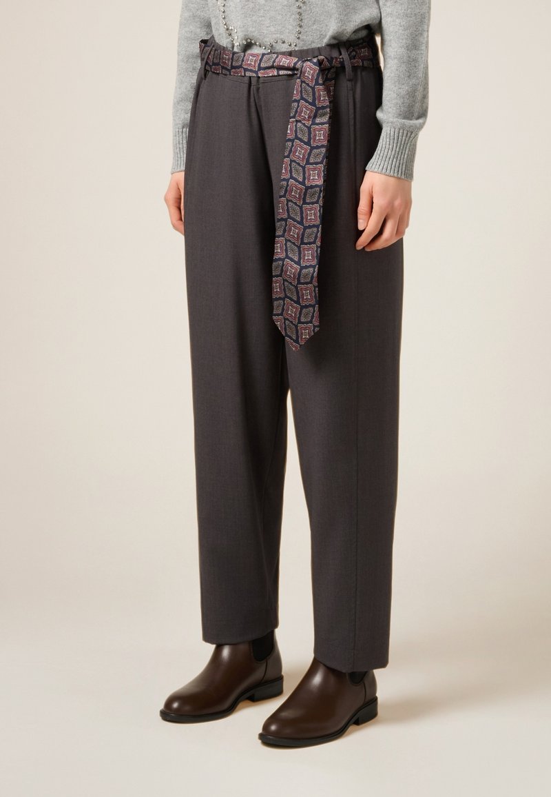 Pantaloni grigi su misura con una cintura larga decorata da una cintura con motivo. Abbinati a stivaletti marroni lucidi. Maglione morbido lavorato a maglia visibile.