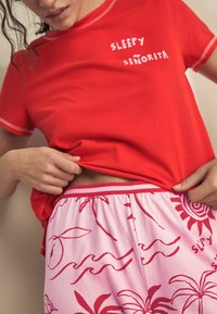 Red cotton T-shirt with "SLEEPY SEÑORITA" text, paired with pink shorts featuring red tropical patterns and a striped waistband.