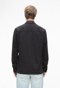 Μαύρο πουκάμισο με μακριά μανίκια, κολάρο, �κουμπωτές μανσέτες και λεπτομέρεια πίσω στον ώμο, σε συνδυασμό με ανοιχτό μπλε τζιν παντελόνι.