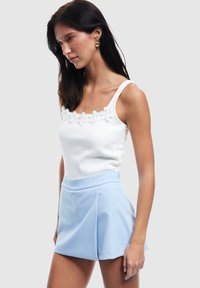 Débardeur blanc à côtes avec broderie florale au niveau de l'encolure, associé à un short plissé bleu clair. Tissu lisse et coupe ajustée.