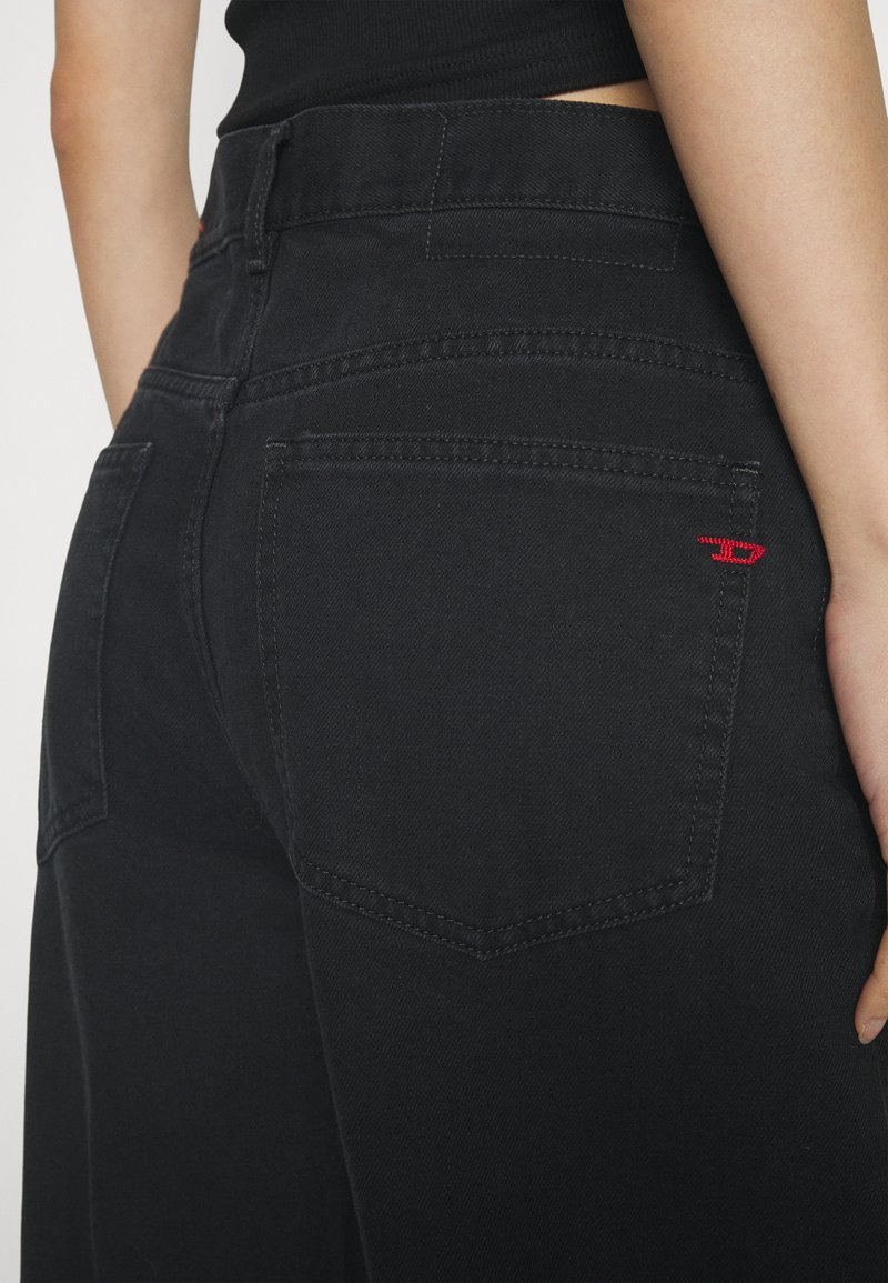 Schwarze Denim-Jeans mit hoher Taille, zwei Gesäßtaschen mit einem roten Logoakzent und kontrastierenden Nähten für zusätzliche Details.
