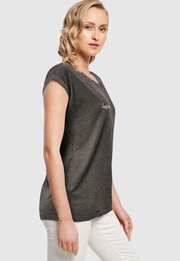 Grå t-shirt med korte ærmer og V-hals med teksten "Inspire" foran. Blødt stof, afslappet pasform, parret med hvide bukser.