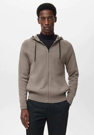 Sudadera con cremallera de color marrón claro, con capucha, dos bolsillos laterales, cordones oscuros y puños ajustados. Fabricada con una tela suave y lisa.