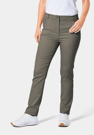 Pantalons vert olive ajustés, dotés de poches avant et d'une fermeture à bouton. Texture lisse, associés à des chaussures de sport blanches.