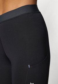 Leggings de sport noirs avec une texture lisse, dotés d'une large taille et d'une poche latérale. Un subtil détail de couture est visible.