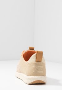 Beige Canvas Slipperschuh mit strukturierten Seiten, oranger Innensohle und brauem Ziehschlaufe. Gepunktete weiße Sohle. TOMS-Logo auf der Rückseite.