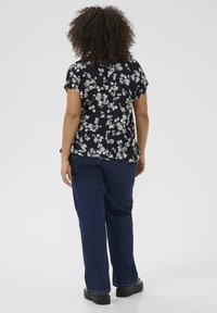 Blusa a maniche corte con stampa floreale in blu navy, con fiori di colore chiaro; indossata con jeans blu scuro e scarpe con tacco nero.