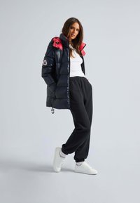 Puffjacka i glänsande svart med röd krage, kombinerad med svarta sweatpants och vita sneakers. Har sidofickor och elastiska manschetter.