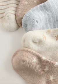 Vijf paar babysokken in beige, grijs en wit met strepen, stippen en konijnenpatronen, gerangschikt in een waaier op een lichte achtergrond.