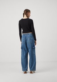 Top corto negro de manga larga combinado con pantalones cargo de denim azul holgados que cuentan con bolsillos laterales y una cinturilla elástica.