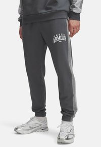 Grå joggere lavet af blødt stof, med elastisk talje, afsluttede ankler, sidelogo i lysere grå og et hvidt logo.
