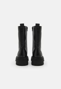 Černé kožené kotníkové boty s hladkou texturou, s masivní podrážkou a bočními zipy pro snadné oblékání, navržené v minimalistickém stylu.