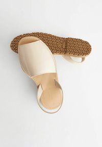 Sandali beige chiaro con una larga fascia anteriore e un manico posteriore, dotati di una suola in gomma marrone texturizzata e una tomaia in pelle liscia.