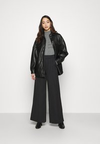 Svart skinn knapp-jakke, grå turtle-neck under, høyt liv svart vide bukser, ankelstøvler, langt bølgete hår.