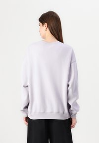 Ljuslila sweatshirt, mjukt tyg, avslappnad passform, ribbade mudd och nederkant, sänkt axelparti, minimalistisk design, kombinerad med svarta byxor.