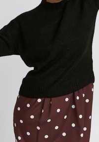 Un pull noir en maille avec un col rond et des poignets côtelés, associé à une jupe bordeaux à grands pois blancs.