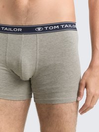 Närbild av en man som bär ljusgrå boxershorts med mörkblå midja som är märkt "Tom Tailor."