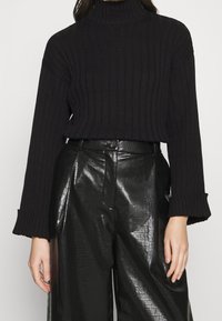 Svart ribbad turtlenecktröja med långa ärmar, kombinerad med högmidjade blanka svarta läderbyxor med krokodilmönster.