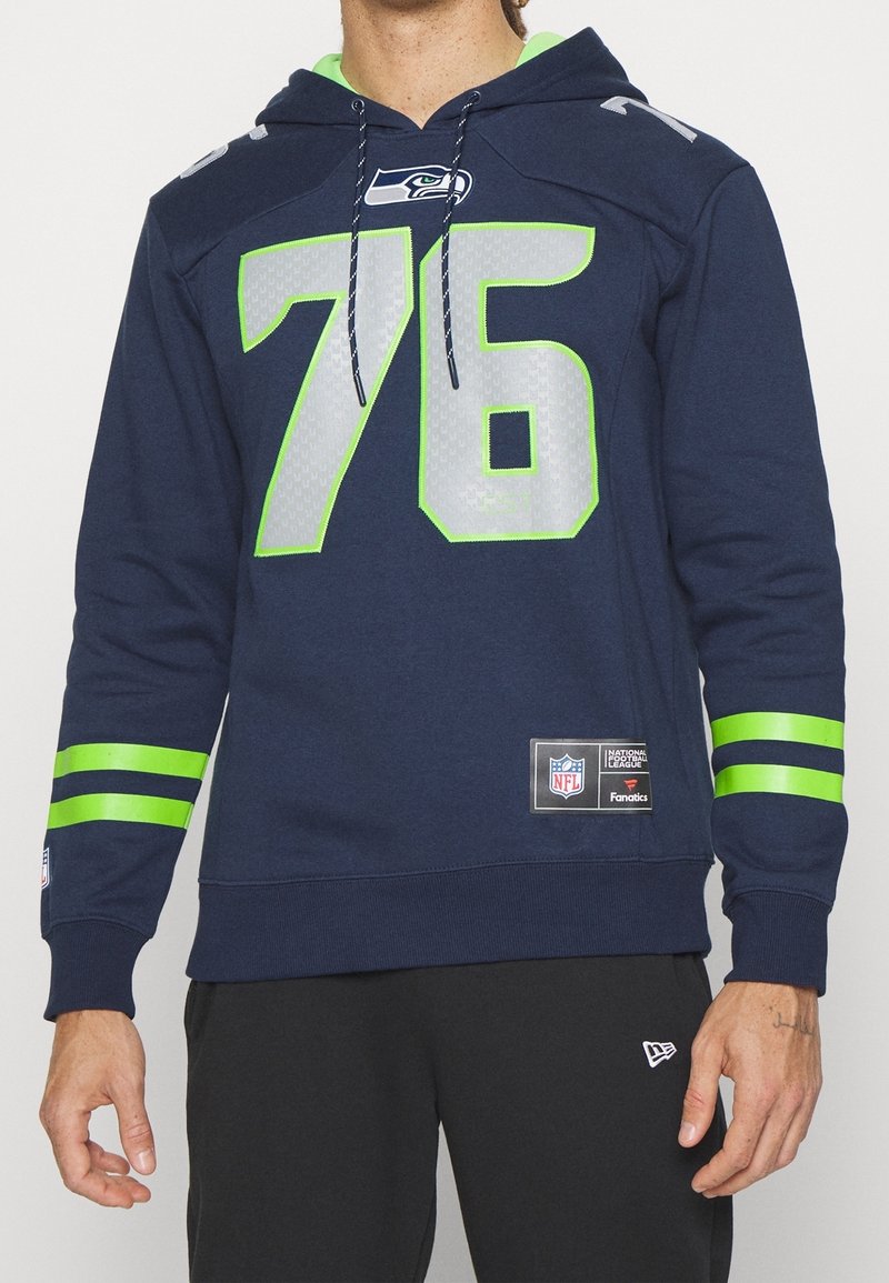 Sweat à capuche bleu marine des Seahawks avec le numéro 76 vert néon et des rayures sur les manches, porté par une personne debout portant un pantalon noir.