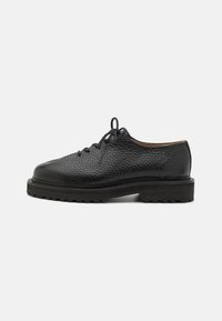 Chaussures noires en cuir à lacets avec une surface texturée, bout rond et semelle en caoutchouc épaisse dotée d'un motif de bande de roulement pour une meilleure adhérence.