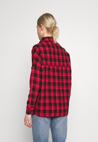 Red and black checked shirt made of fabric, featuring a collar, button cuffs, and a relaxed fit. Displayed from the back.