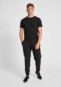 Black cotton crew neck t-shirt, paired with black sweatpants featuring cuffed ankles. Black athletic shoes complete the outfit.