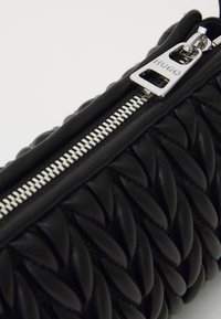 Pochette en cuir noir avec motif tissé texturé et matériel de fermeture éclair en argent. Logo sur la tirette de la fermeture éclair. Fini lisse dans l'ensemble.