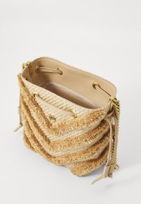 Tanny geweven strooien tas met een franjertextuur, voorzien van gouden hardware, een trekkoordsluiting en een gladde beige voering.