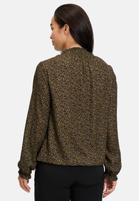Blusa marrone con motivo, maniche lunghe, collo smock e polsini elastici, caratterizzata da una stampa leopardata su uno sfondo scuro.
