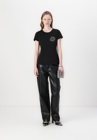T-shirt nero a maniche corte con un design grafico circolare sul davanti, abbinato a pantaloni neri in ecopelle a vita alta e scarpe nere lucide.