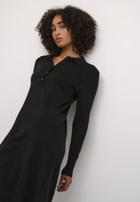 Black long-sleeve dress with a polo collar, featuring a button placket, smooth texture, and fitted silhouette, against a plain white background.