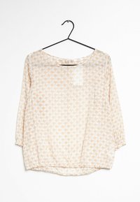 Blouse légère et transparente en beige doux avec un motif géométrique de formes orange clair, col rond et manches trois-quarts.