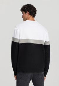 Felpa da uomo in nero, grigio e bianco. Presenta un design a blocchi di colore con una texture liscia e polsini a costine. Stile classico a girocollo.