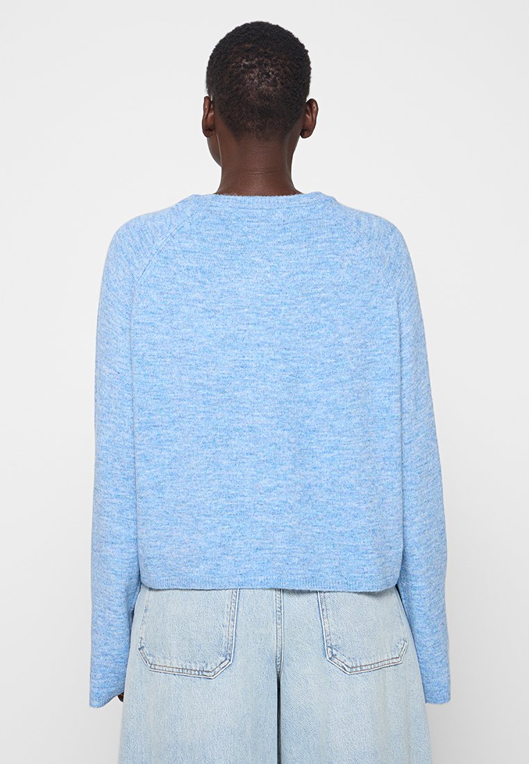 Hellblauer, strukturierter Pullover mit rundem Ausschnitt und langen Raglanärmeln, kombiniert mit hochgeschnittenen hellen Jeans.