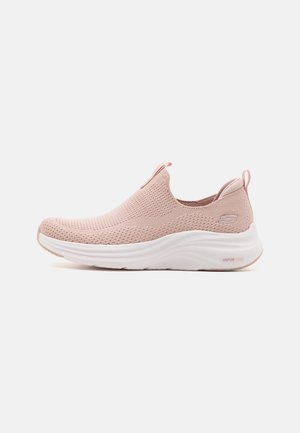 Zapatilla deportiva rosa claro sin cordones con parte superior de tejido transpirable, suela blanca gruesa con etiqueta "Vapor Foam" y logo de la marca en el lateral del talón.