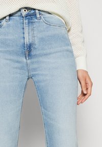 Ljusblå denimjeans med hög midja, med subtila blekningar, klassisk femficksdesign och dragkedjeöppning med metallknappslut.