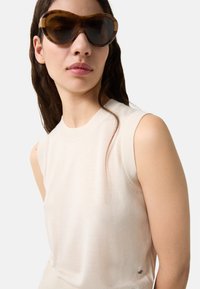 Beige bezramenný top s žebrovaným výstřihem, který předvádí hladkou strukturu. Hnědé oversized sluneční brýle s kulatým designem a tmavými čočkami.
