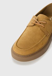 Lace-up casual shoe made from textured mustard-yellow suede with a rounded toe, stitched accents, and a beige rubber sole.