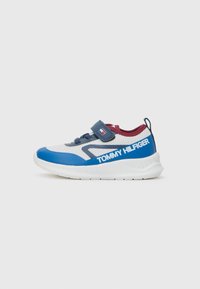 Zapatilla azul y blanca con parte superior de malla texturizada, tira de velcro y suela de goma. Presenta el logo "TOMMY HILFIGER" en el costado.