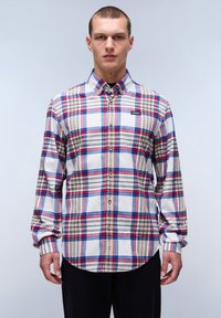 Camisa de botones con base blanca que presenta un patrón de cuadros en rojo, azul y beige. Material de algodón, mangas largas y dobladillo curvado.