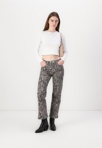 Haut blanc à manches longues cropped avec le logo "HUGO", associé à un pantalon texturé en imprimé serpent et des bottes noires à talons. Le pantalon dispose de poches latérales.