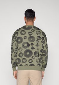 Φούτερ σε ελιά πράσινο με μαύρο κυκλικό ανθικό σχέδιο, με μανσέτες και τελείωμα σε ριμπ ύφανση, λαιμόκοψη σε στυλ 'crew' και άνετη εφαρμογή.