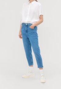 Světlé modré rifle s vysokým pasem a rovnými nohavicemi, doplněné bílým tričkem s krátkým rukávem a světlými teniskami.