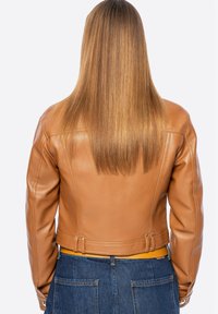 Giacca cropped in pelle marrone con spalle strutturate, texture liscia e due cinturini decorativi sulla schiena. Abbinata a una fascia gialla in vita.
