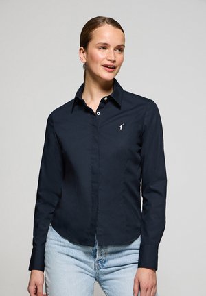 Marineblaue Langarmshirt mit einem Button-down-Kragen, taillierter Passform und kleinen weißen Logodetails auf der linken Brust. Baumwollmischgewebe.